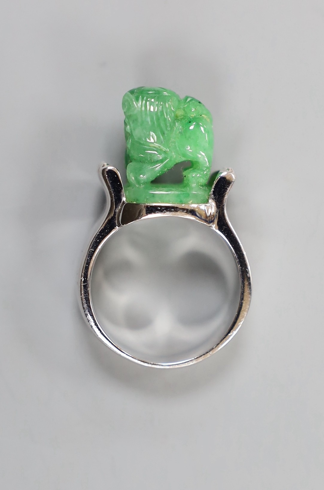 A 585 white metal and jadeite ring, carved with a lion dog, size O, gross weight 11.1 grams.